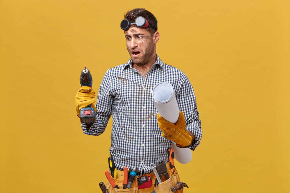 portrait dirty repairman having tool belt holding blueprint drill machine looking it with anger as it works badly craftsman expressing his dissatisfaction with tools instruments